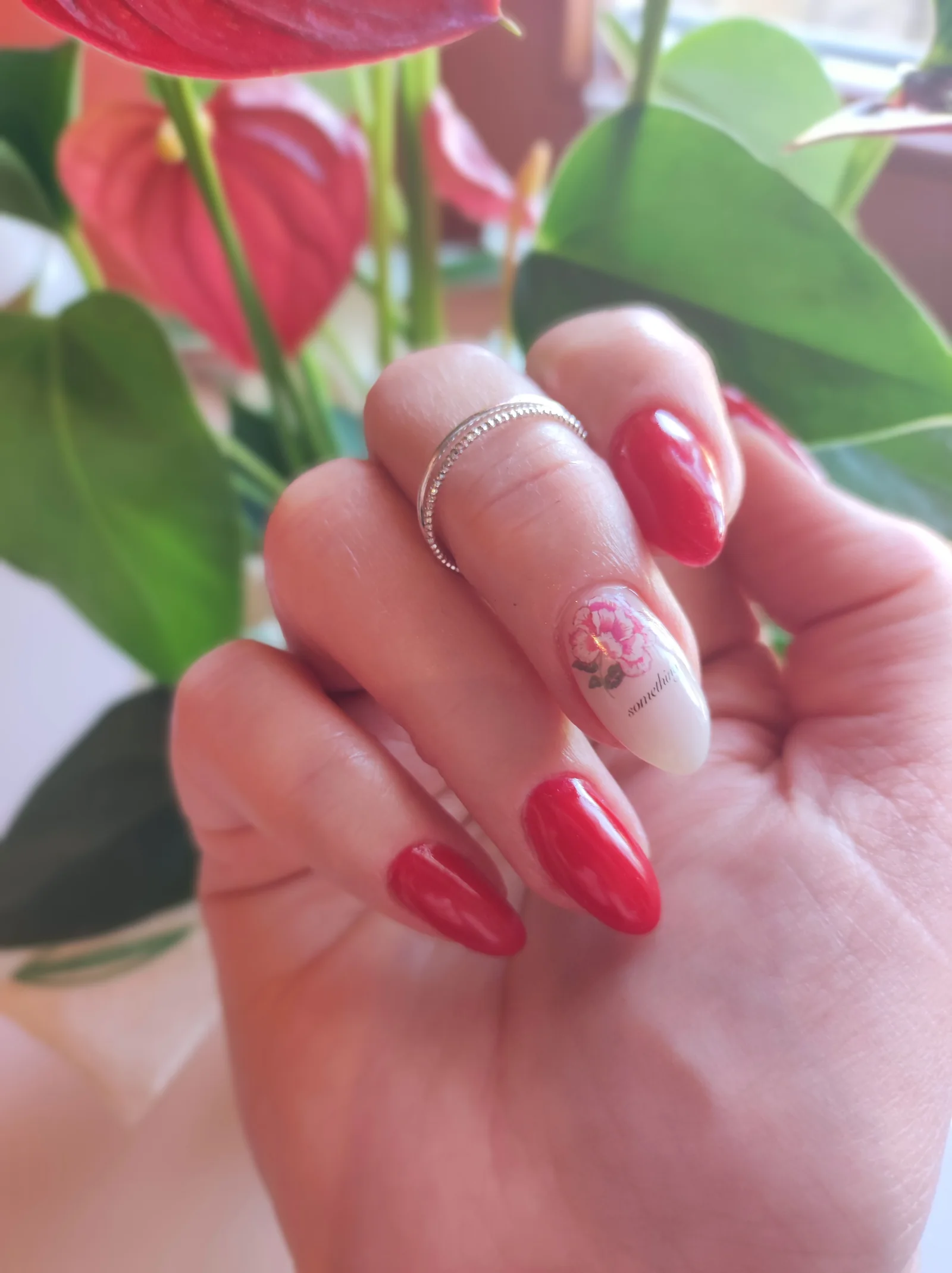 Rot lackierte Nägel mit gemaltem Blütenmotiv auf dem Ringfingernagel